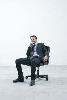 Elegant businessman sitting on an office chair in an empty room looking at camera.