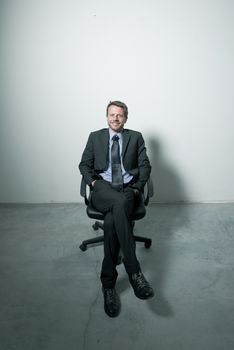 Businessman sitting on an office chair against concrete floor background.
