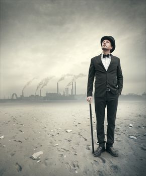 Vintage businessman looking away with polluting factory and post atomic landscape on background.