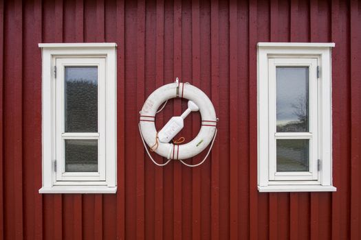 Life buoy on old red wood wall by two white windows.