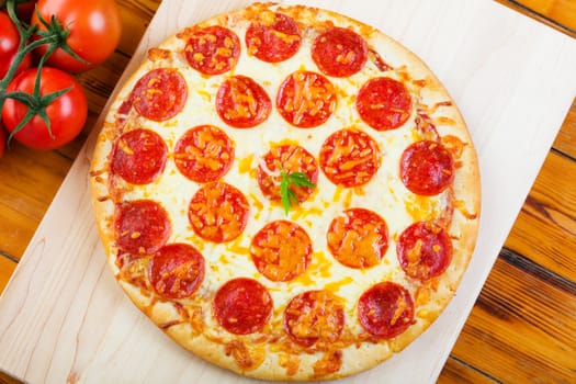 Pepperoni pizza on a wooden board with tomatoes.