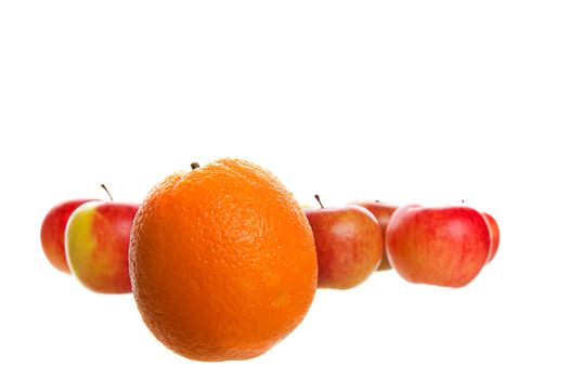 An orange stands out from a crowd of apples.  Shot on white background.