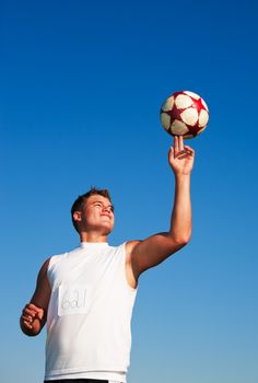 A young man spinning a soccer ball on his finger in the warm summer sun.