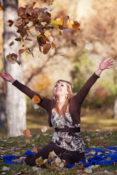 A young woman enjoying the sun on her face and throwing leaves into the air.