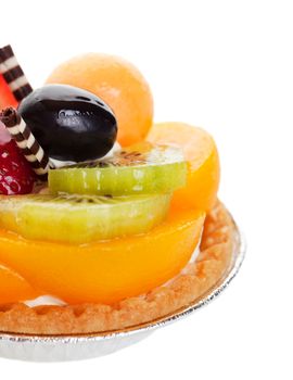 A decadent fruit tart, piled high with fresh fruit, and garnished with two delicate spikes of rolled white and milk chocolate.  Shot on white background with shallow depth of field.