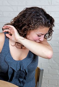 A young woman, sneezing into her elbow to prevent spreading germs.
