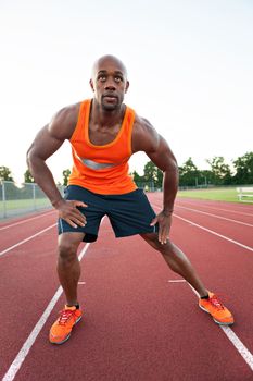 African American man in his 30s stretching at a sports track outdoors.