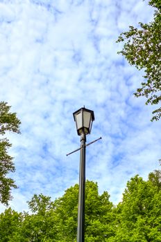 Lamp post in the forest against a cloudy sky