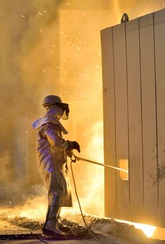 A steel worker takes a sample from oven