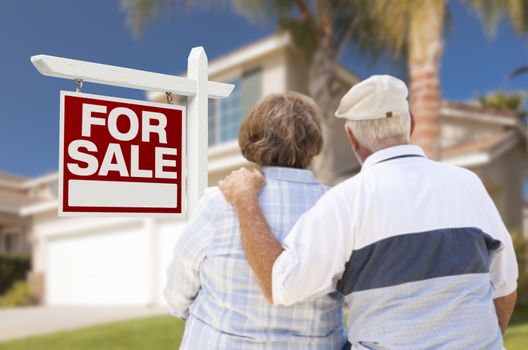 Happy Senior Couple Front of For Sale Real Estate Sign and House.