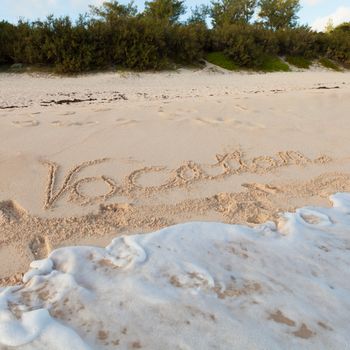 The word Vacation written in the sand on a Bermuda beach with pink sands.