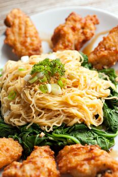 Thai style fried chicken wings on a round white plate with egg noodles and spinach.