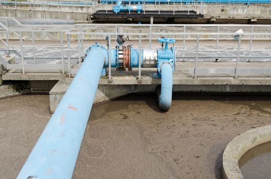 Blue stopcock tap valve gate and pipes in water treatment plant and dirty liquid bubble in background.