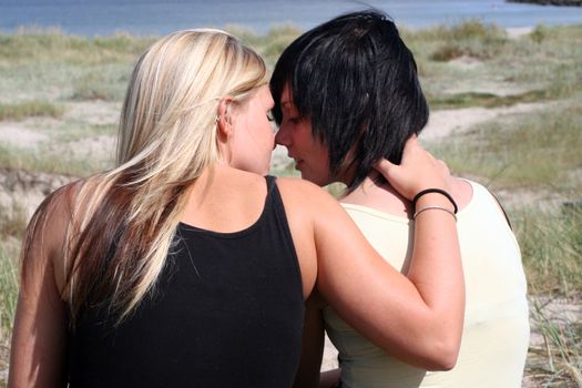 two Young women sitting at the Beach holding each other, flirting and kissing