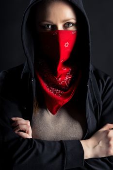 On a black background girl formidable form in black hood with a red shawl on his face