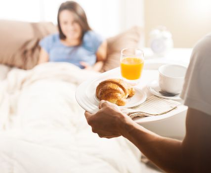 Hand holding breakfast tray to a happy relaxed woman in bed 