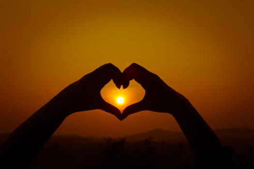 Silhouettes hand heart shaped  with sun sets and the sky orange