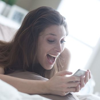 Happy woman at home reading a text message in her bright bedroom 