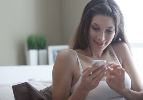 Relaxed woman at home reading a text message in her bright bedroom 