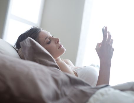 Relaxed woman at home reading a text message in her bright bedroom 