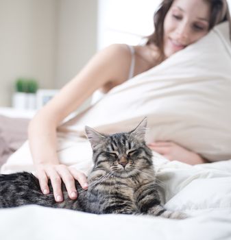 Woman relaxing on bed with her cat on the summer warm day. 