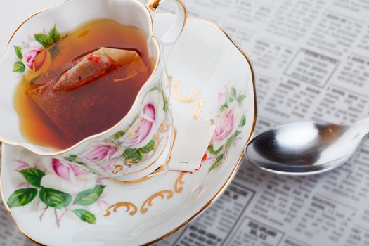 Herbal tea with teabag, in fine china teacup with the morning classifieds.