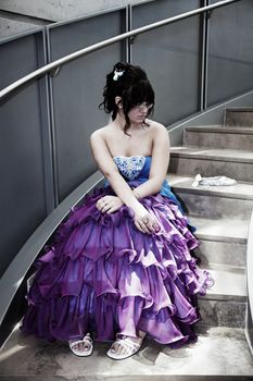 A young girl sits alone in her prom dress on a lonely flight of stairs.