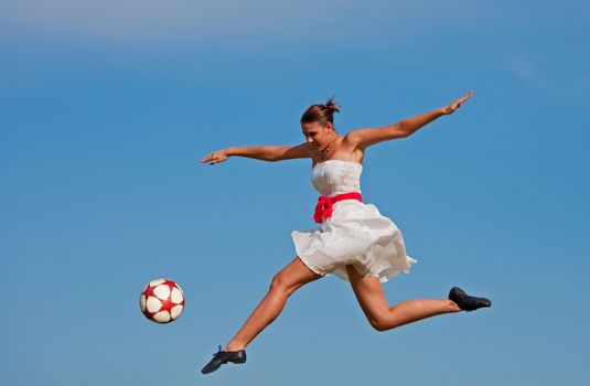 A beautiful girl kicking a soccer ball with the grace of a ballet dancer.