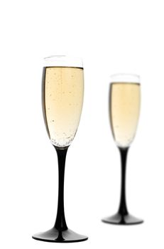 Two black-stemmed wine flutes filled with champagne.  Focus on first glass.