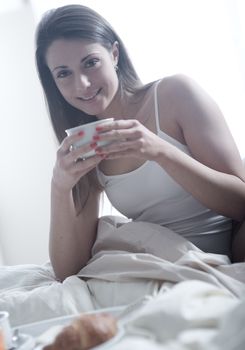 Lovely young woman lying with a cup of coffee and a tray of breakfast 