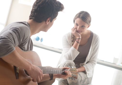 Young handsome man playing guitar for his girlfriend