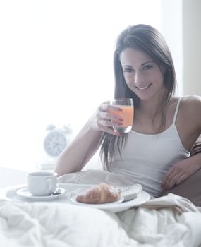 Lovely young woman lying with a glass of orange juice and a tray of breakfast 