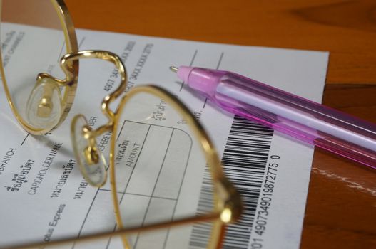 Monthly credit card statement placed on the table with pen and gold Glasses.                             