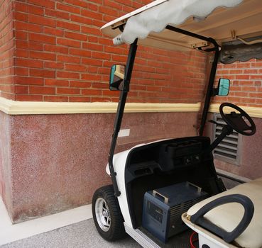 Small white golf car with a roof, parked beside a brick wall.                               