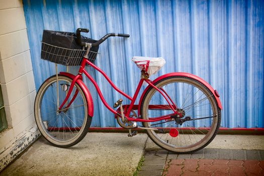 Old, 1950's era, red bike leaning against a blue wall.