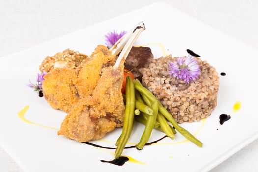 Mixed meat dish with green beans and buckwheat porridge with mushroomson white decorated plate.