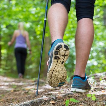 Young fit couple hiking in nature. Adventure, sport and exercise. Detail of male step, legs and nordic walking poles in green woods.