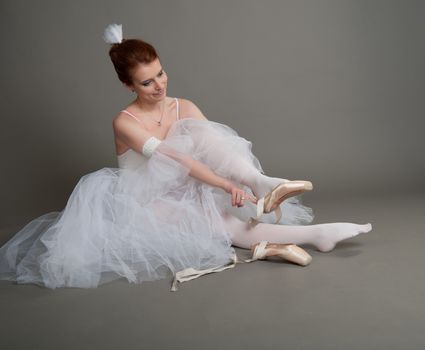 dancer wears pointes,sitting on the floor on a grey background