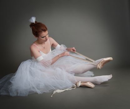 dancer wears pointes,sitting on the floor on a grey background