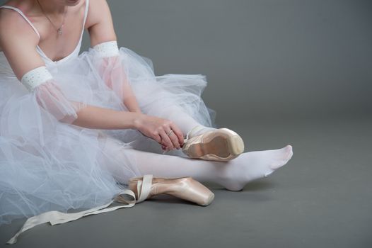 dancer wears pointes,sitting on the floor on a grey background