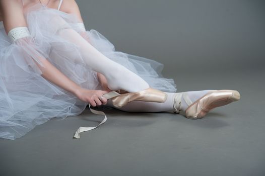 dancer wears pointes,sitting on the floor on a grey background