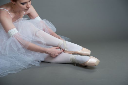 dancer wears pointes,sitting on the floor on a grey background