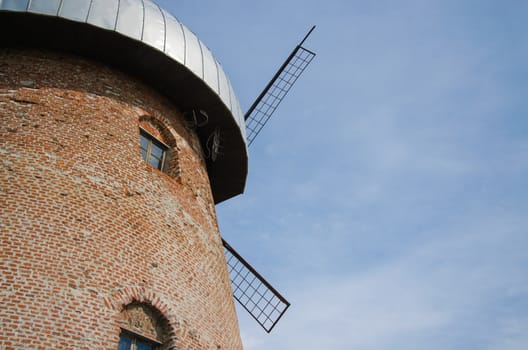 side of rustic old windmill with small window on blue sky background