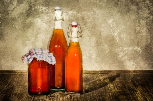 Bottles filled with yellow syrup and jam on kitchen table in vintage style