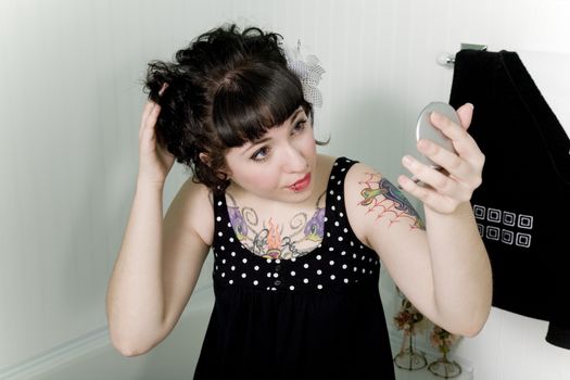 Rockabilly pinup girl looking into a compact mirror and fixing her hair.
