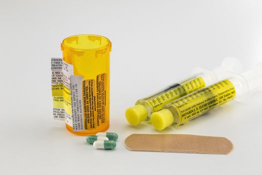 Precription bottle with many adverse reaction warnings. Syringes, bandage, and pill capsules on the side. 