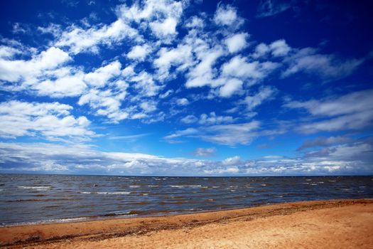 The sky with clouds and a beach. Landscape with the lake. Sunny day on the lake. Beautiful landscape. Sandy beach and waves.