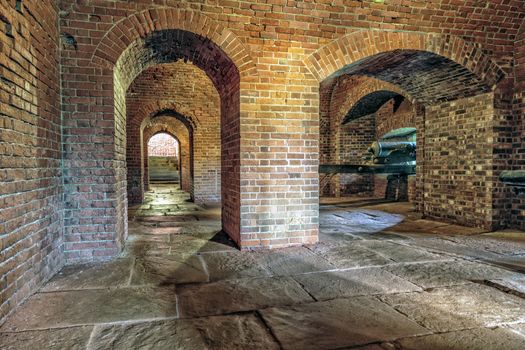 Historic brick archway and tunnel. Antique artillery cannon points out of window.