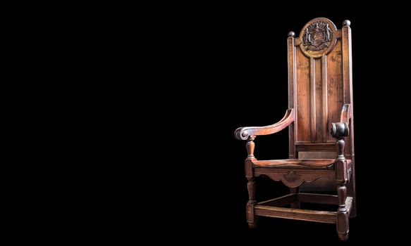 Heavy wooden high backed chair with beautiful scrollwork and craftsmanship. On black background.
