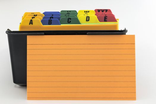 Black plastic box index card filer with colorful alphabetized tabs. Blank orange index card is propped up in front. 